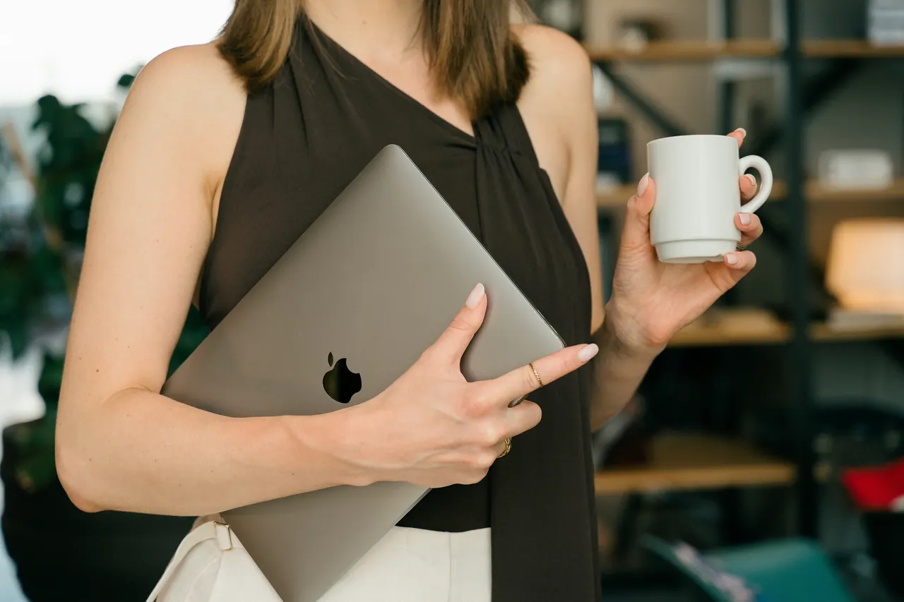 A woman holding her laptop and a cup of coffee